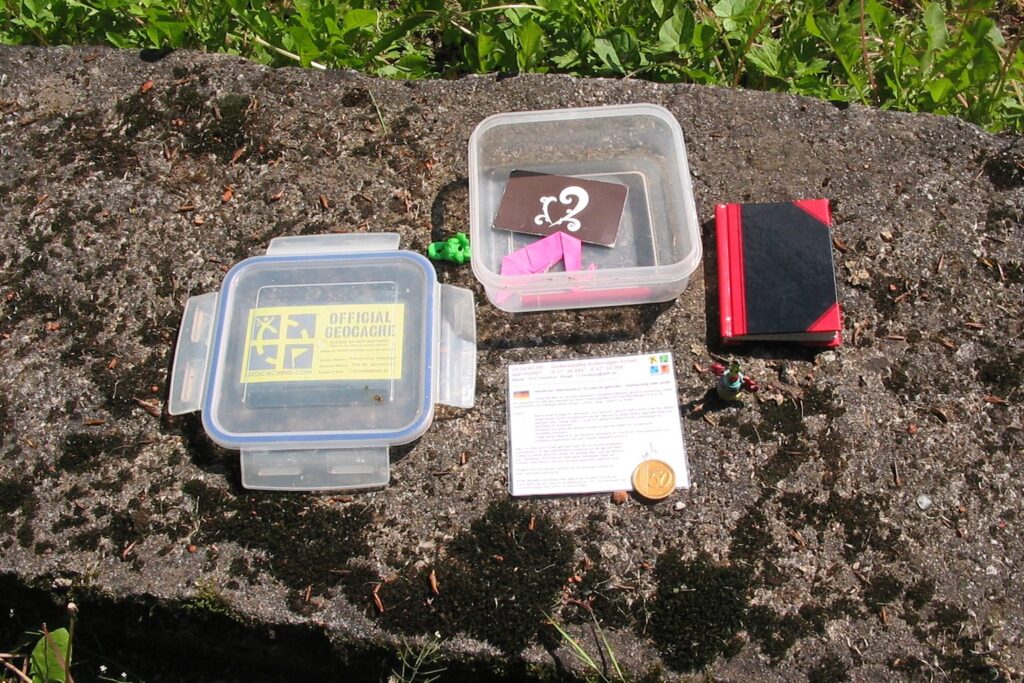 Geöffnete Geocache-Dose mit Logbuch, Stift und Tauschgegenständen