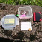 Geöffnete Geocache-Dose mit Logbuch, Stift und Tauschgegenständen