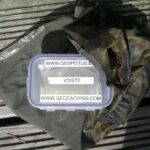 Geocache-Dose mit Beschriftung auf einem Tarnnetz auf Holzplanken
