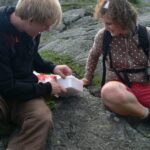 Zwei Geocacher sitzen auf einem Felsen und öffnen eine gefundene Cache-Dose