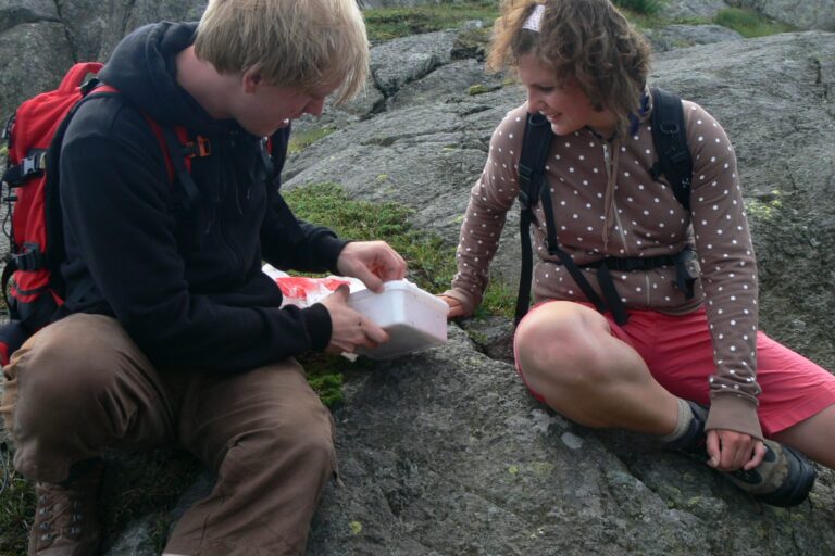 Zwei Geocacher sitzen auf einem Felsen und öffnen eine gefundene Cache-Dose