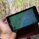 Hand hält ein Tablet mit Navigationskarte im Wald