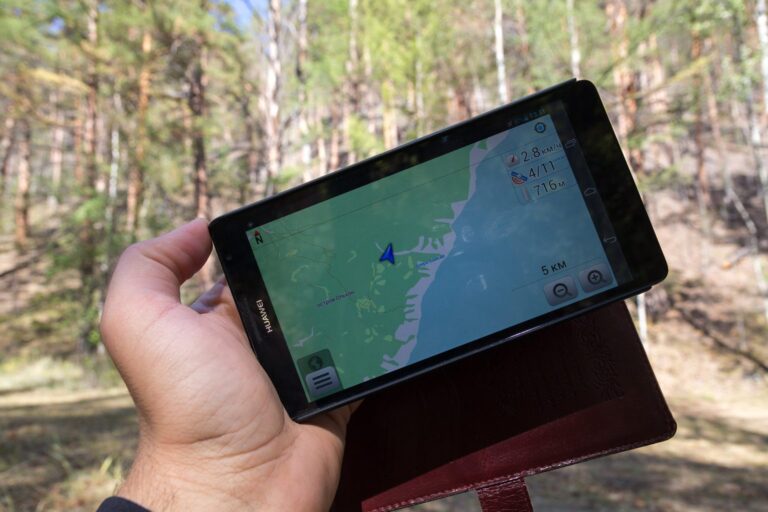 Hand hält ein Tablet mit Navigationskarte im Wald