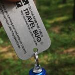 Travel-Bug-Anhänger mit Tracking-Nummer vor einem Wald