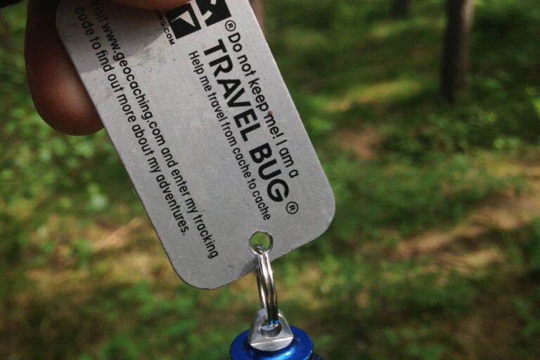 Travel-Bug-Anhänger mit Tracking-Nummer vor einem Wald