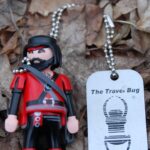 Spielfigur mit Travel-Bug-Anhänger auf Laub im Wald